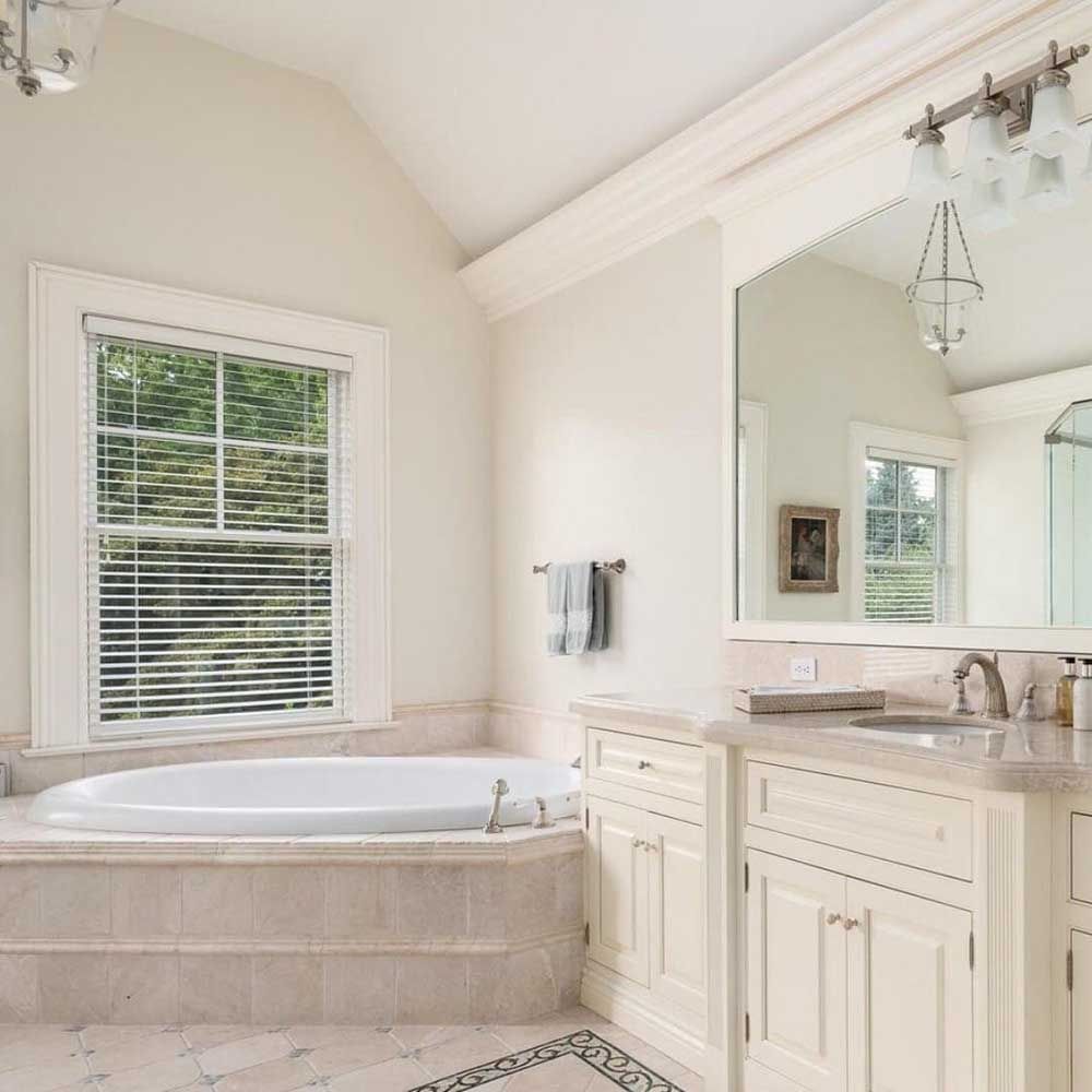 A bathroom with a tub , sink , mirror and window