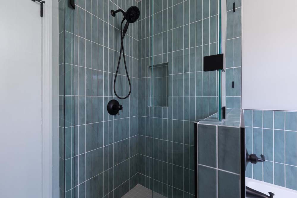 A bathroom with blue tiles and a walk in shower with a glass door.
