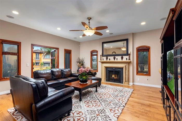 A living room with a couch , chair , coffee table , fireplace and ceiling fan.