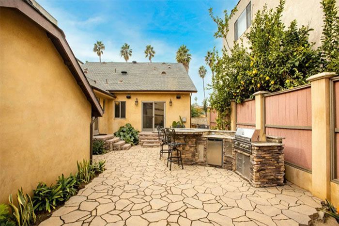 A patio with a grill and a table in the backyard of a house.