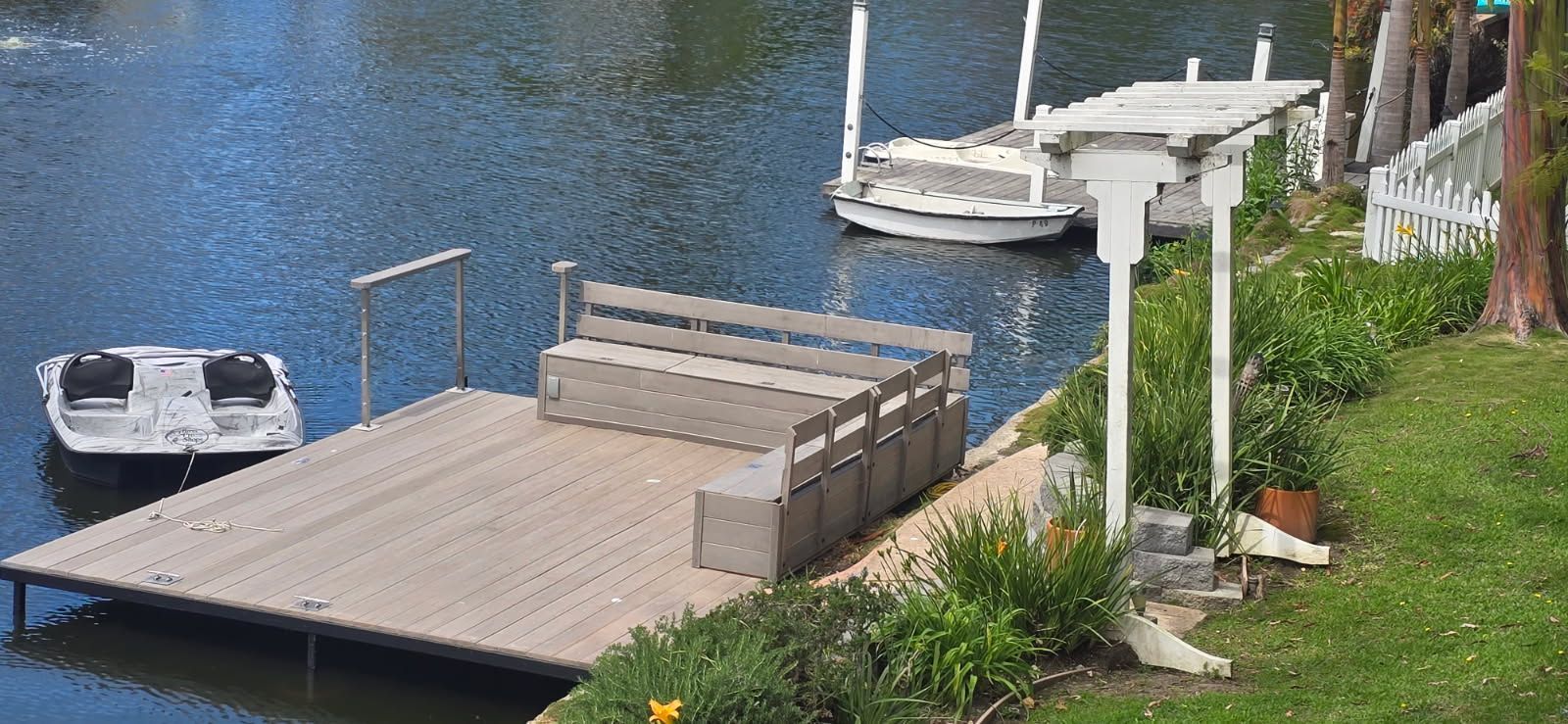 Living room with white sofas, wooden coffee table, and large windows overlooking a backyard.