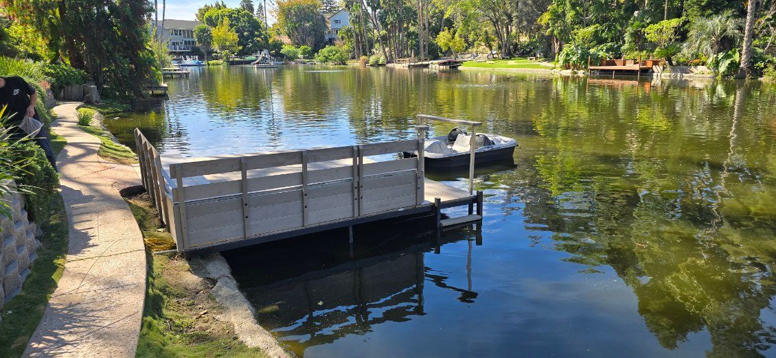 A wooden dock extends into a calm, green lake surrounded by lush trees under a clear sky.