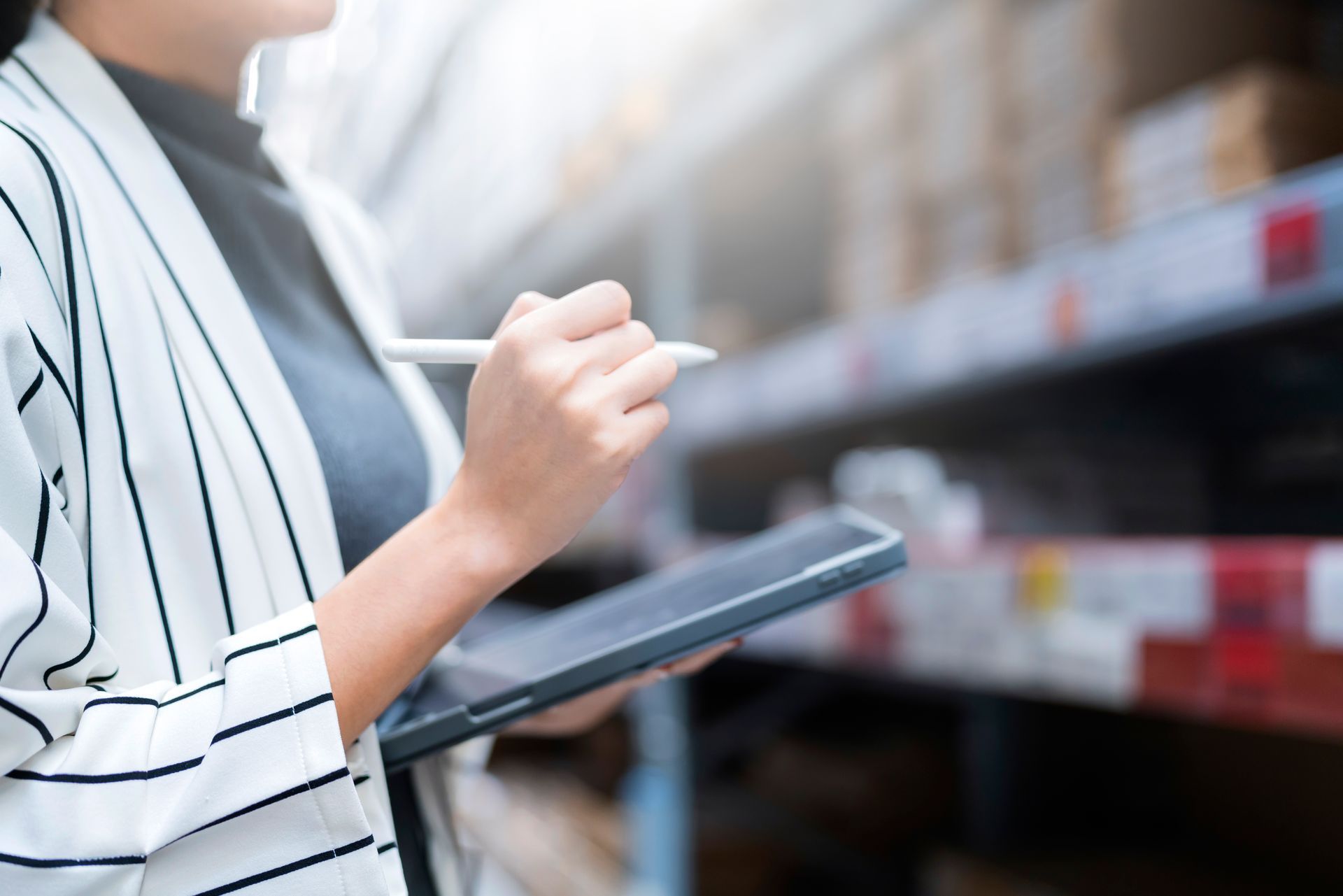 A woman is holding a tablet and a pen in a warehouse.