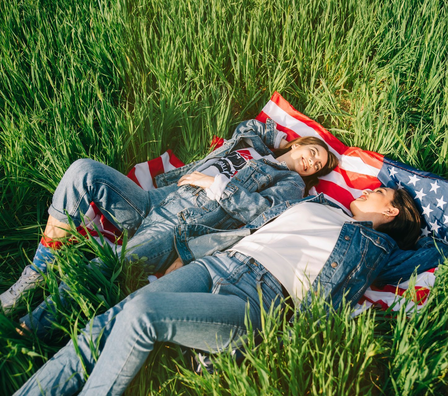 Two women are laying on an american flag in the grass.