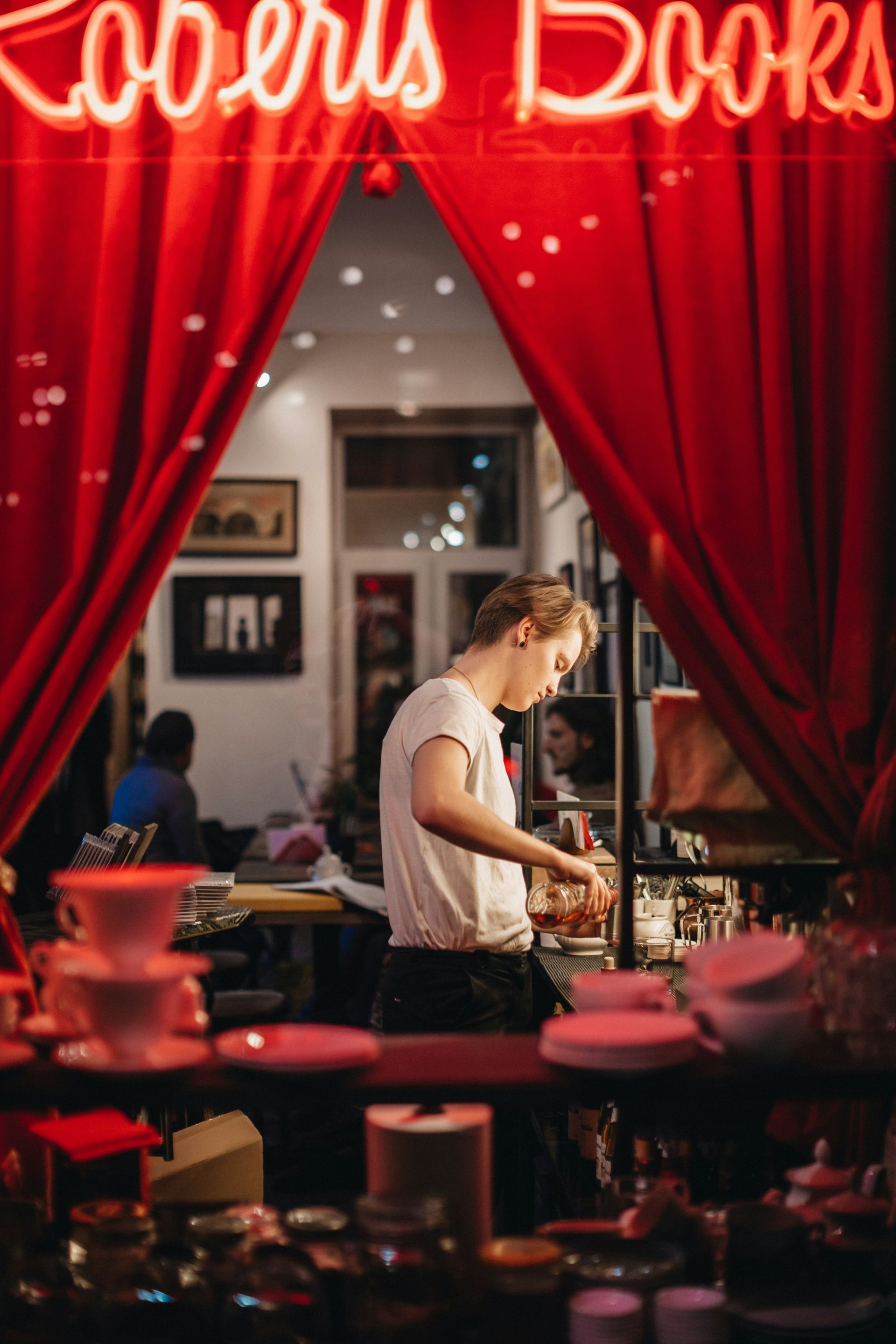 A man is standing in front of a red curtain with a neon sign that says lovers books