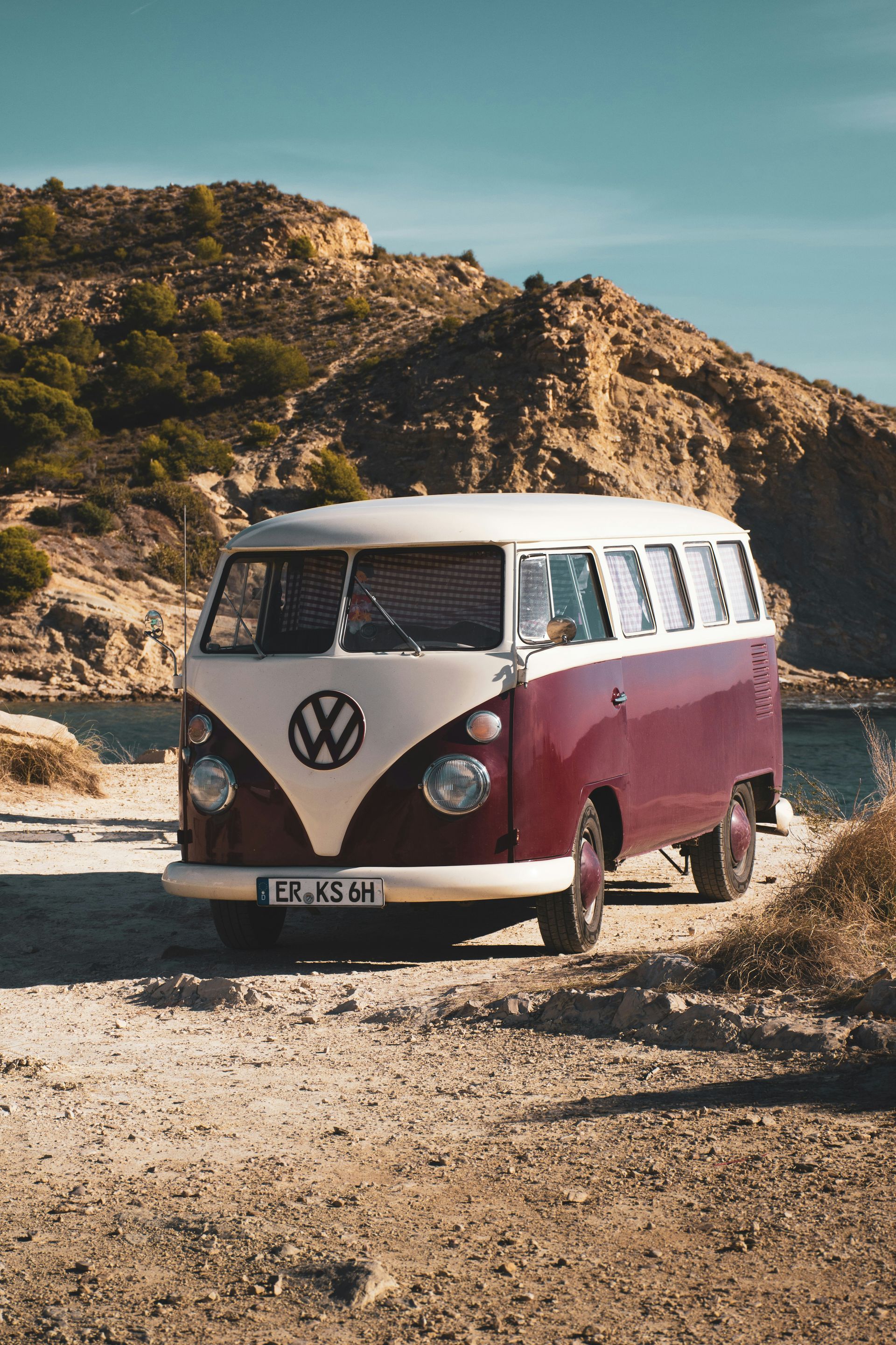 A red and white van is parked on a dirt road next to a body of water.