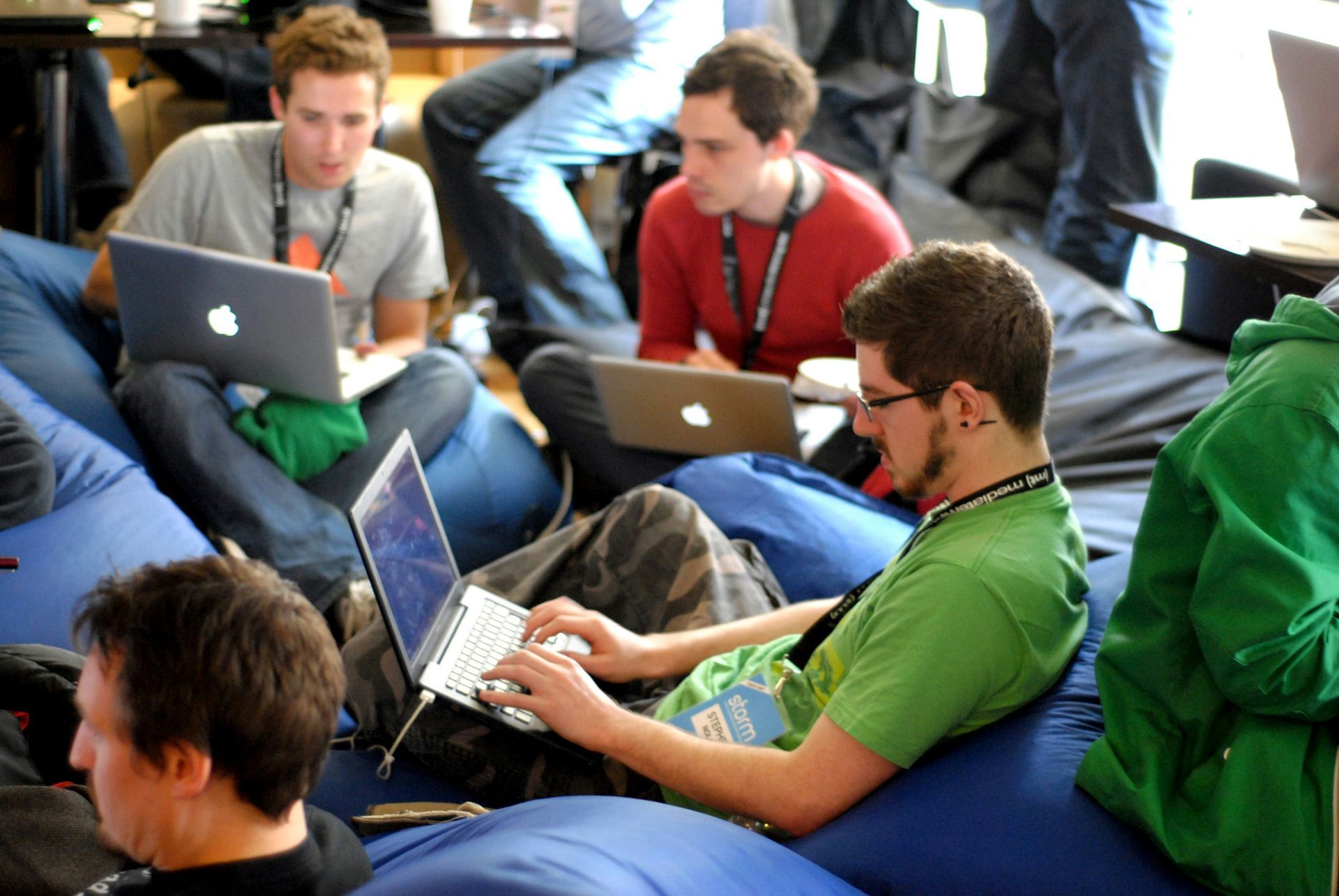 A group of men are sitting on bean bags using laptops