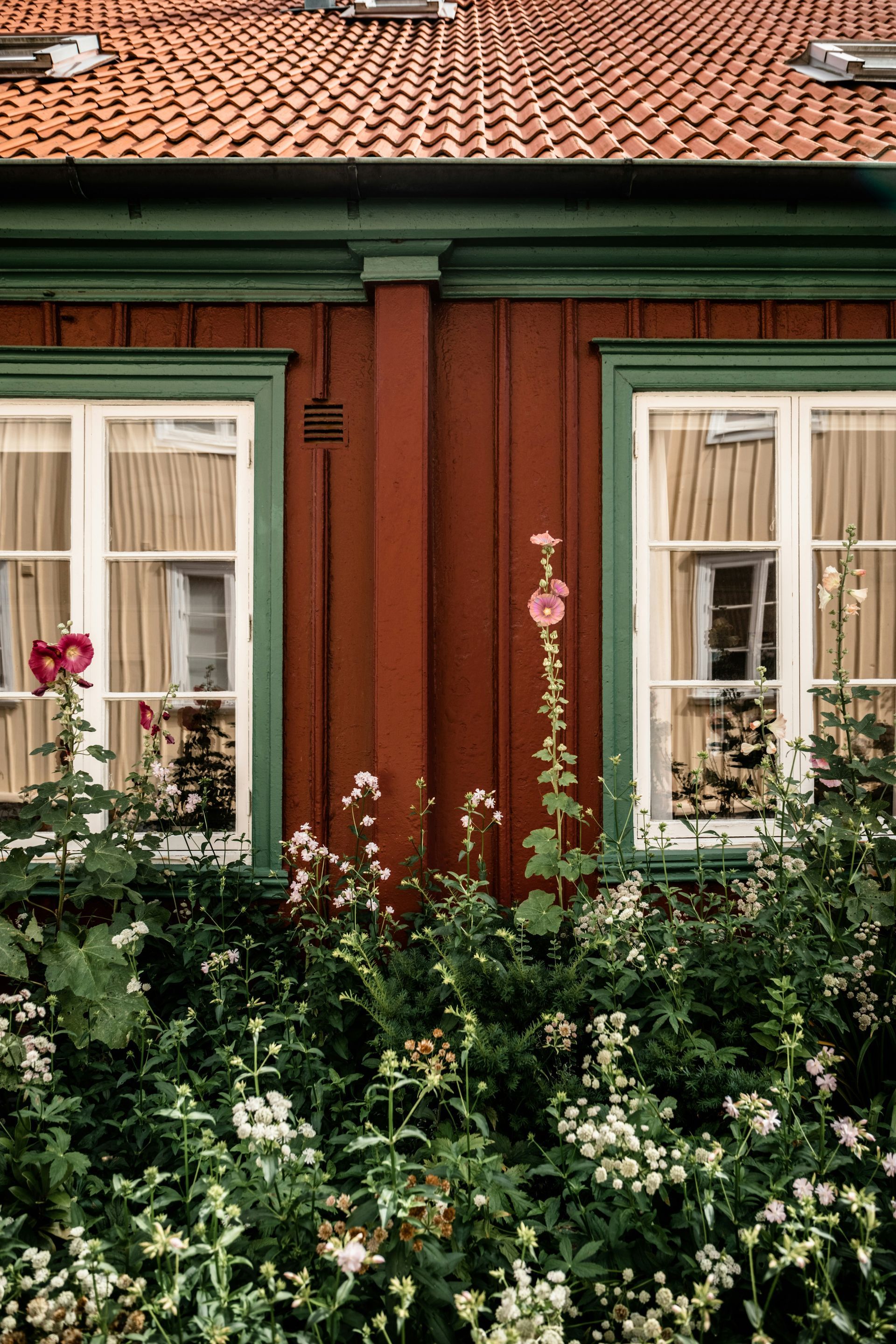 A red house with green windows and flowers in front of it.