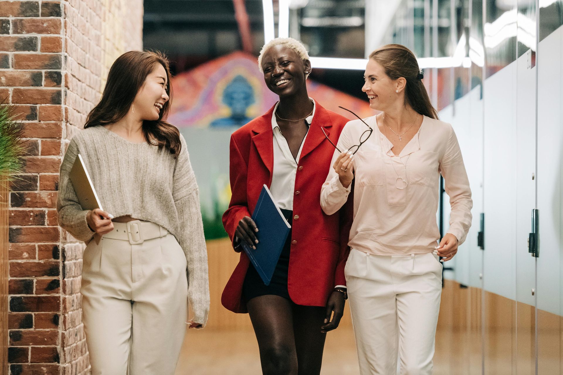 Three women are walking down a hallway and talking to each other.