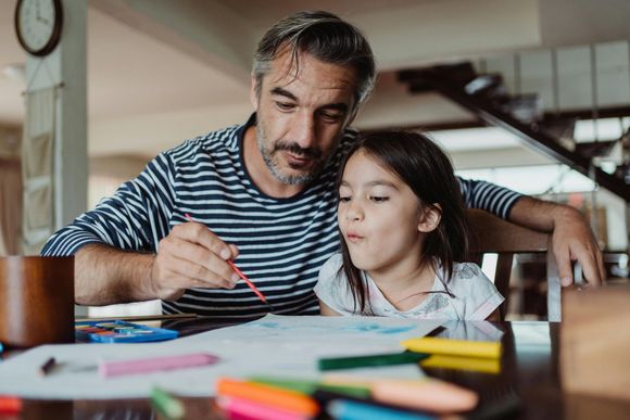 A man and a little girl are sitting at a table drawing with markers.