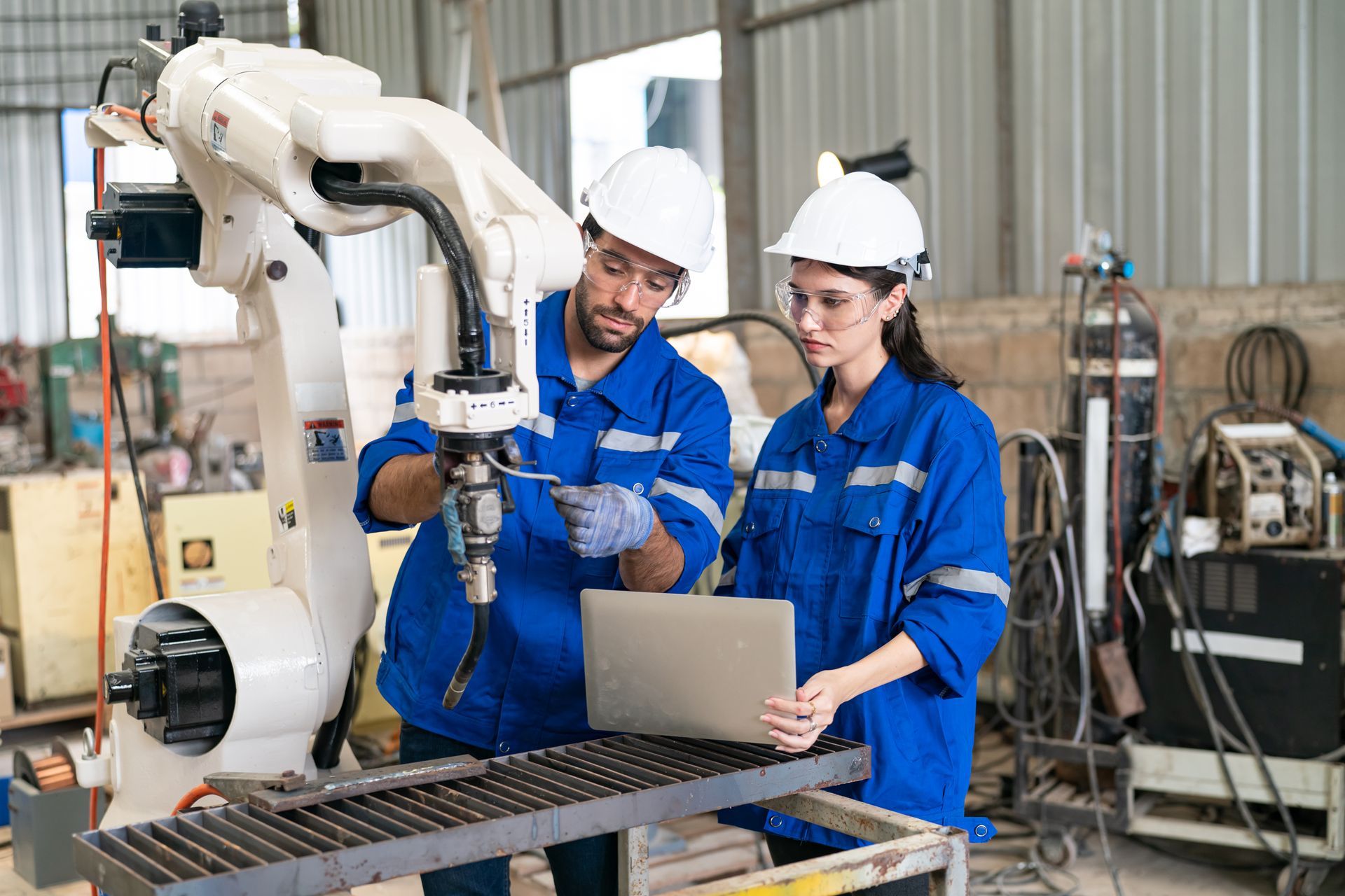 A man and a woman are working on a robot in a factory.