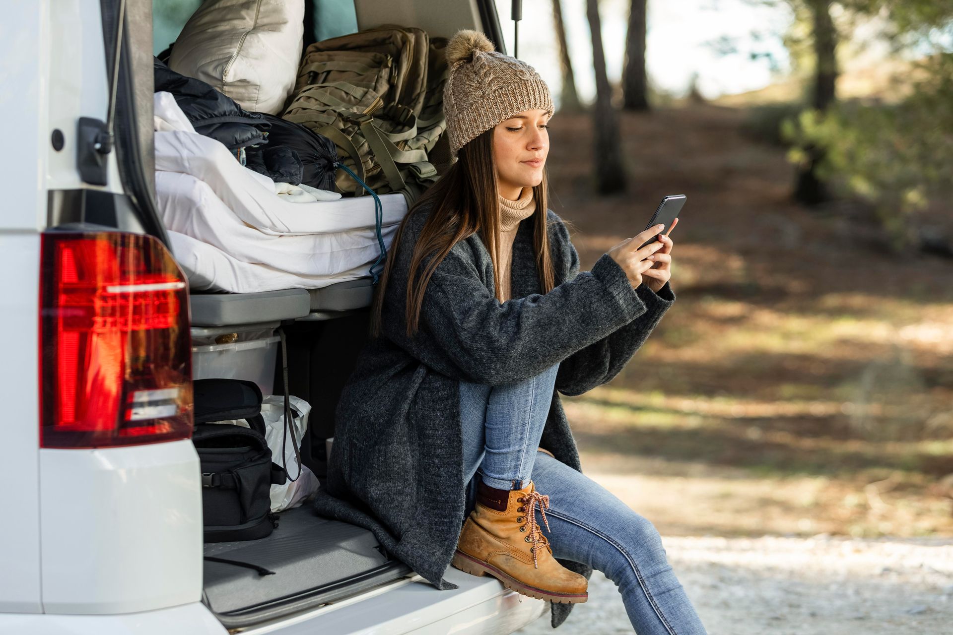 A woman is sitting on the back of a van looking at her phone.