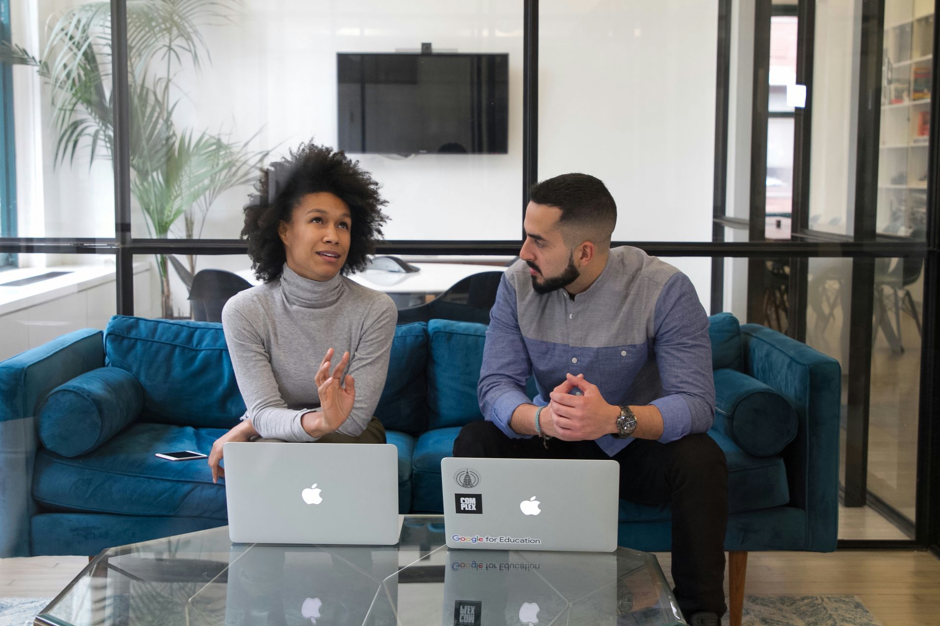 A man and a woman are sitting on a couch with laptops.