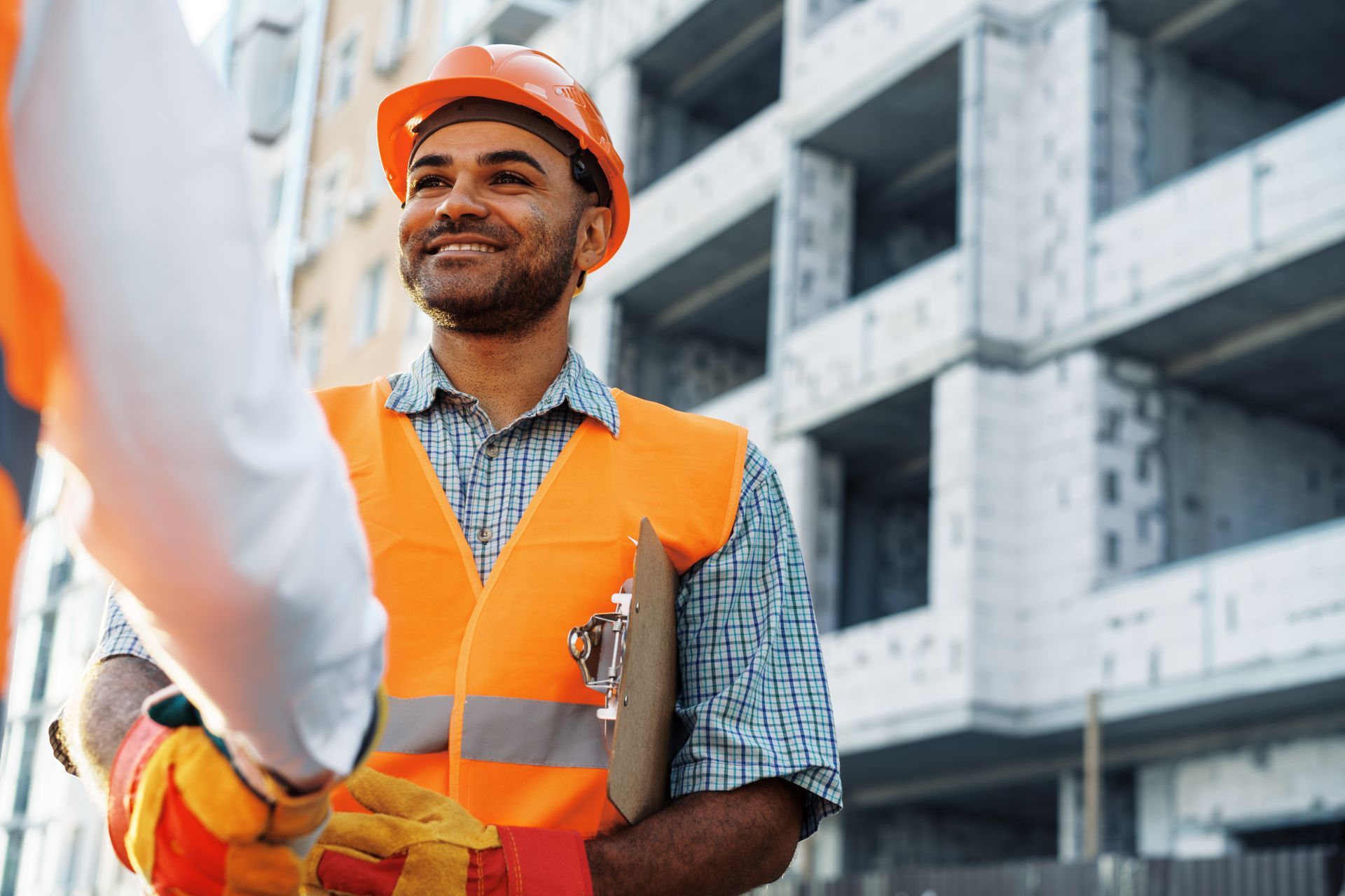 Two construction workers are shaking hands in front of a building under construction.