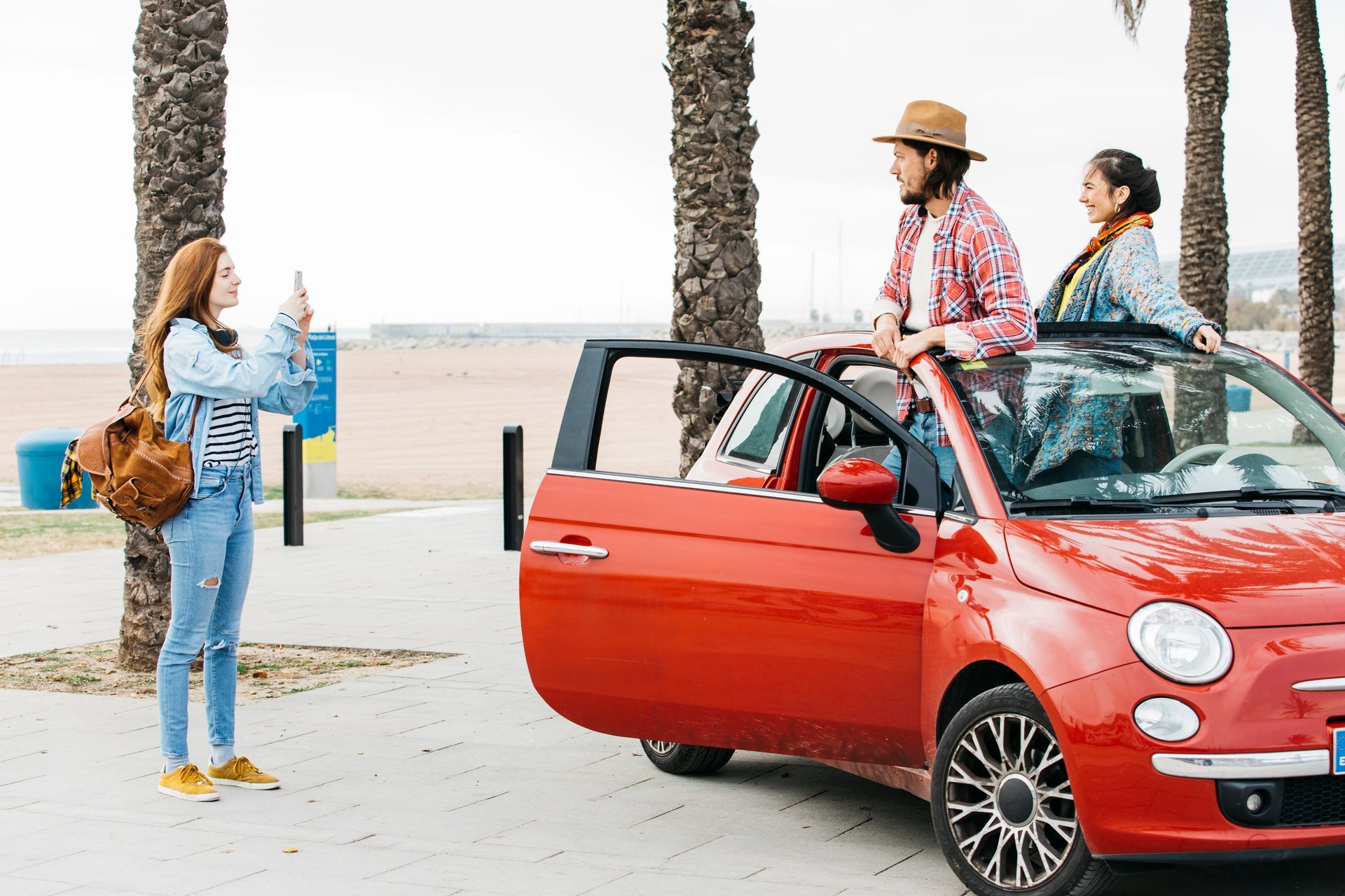 A group of people are standing next to a red car.