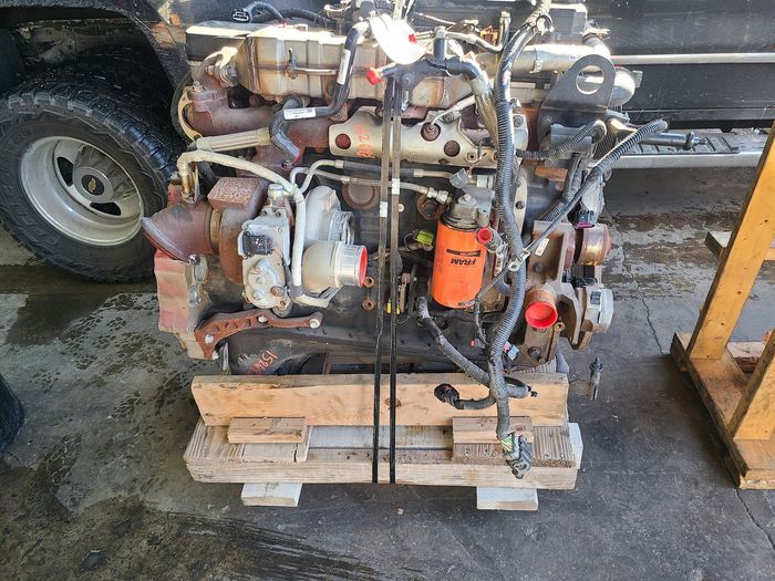 Rusty engine mounted on a wooden pallet beside a truck wheel, with an orange filter attached. | Kingsley Auto Service