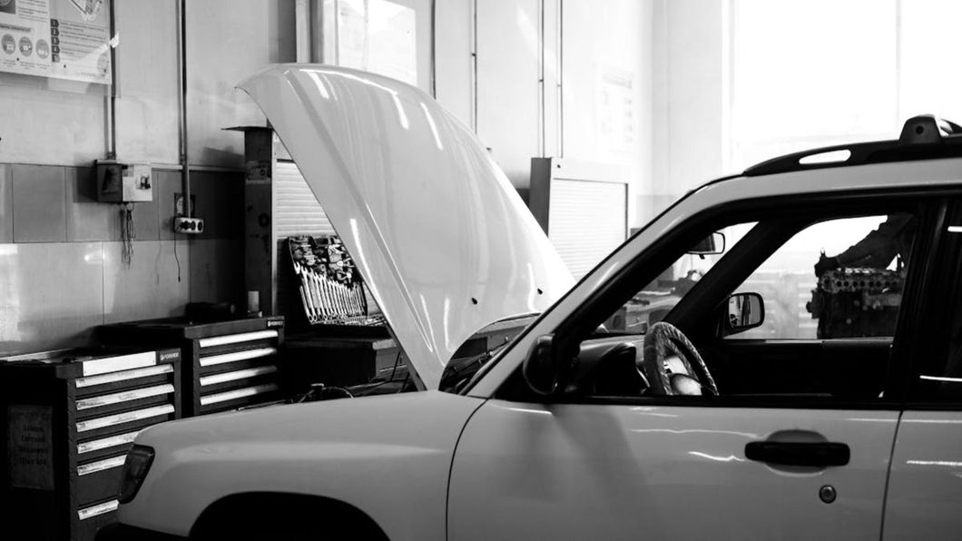Coche blanco en un taller mecánico con el capó abierto, junto a una caja de herramientas y un banco de trabajo.