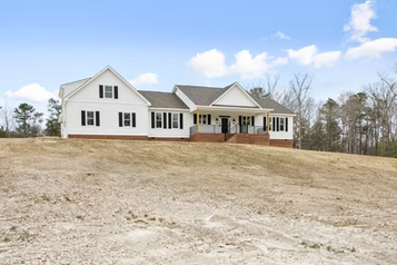 White house with black shutters on a grassy hill under a blue sky.