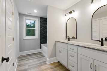 Bathroom with white vanity, black accents, two arched mirrors, window, and gray walls.