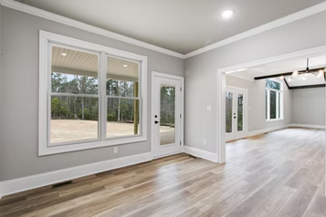 Empty room with light gray walls, white trim, large windows, and wood-look flooring.