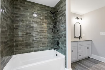 Bathroom with gray brick-style tiled shower, white tub, gray vanity, and wood-look flooring.