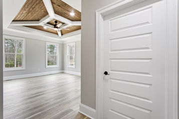 White door with black handle in front of a bedroom with light wood flooring, gray walls, and a wood ceiling with a fan.