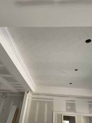 White ceiling with decorative molding, recessed lights, and visible diagonal grid lines in a room under construction.