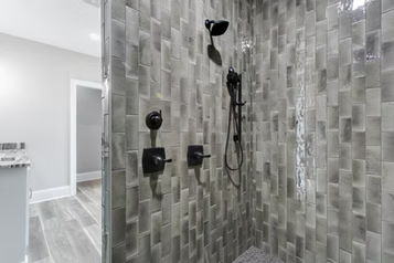 Gray tiled shower with black fixtures; showerhead, controls, and handheld wand.