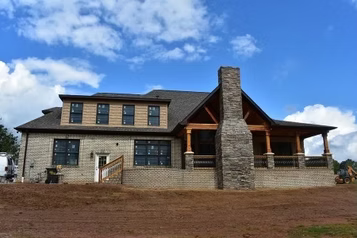 A two-story house under construction with a brick facade and a large covered porch.