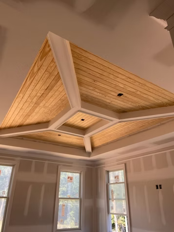 Interior room with unfinished walls and a wood-paneled, coffered ceiling. Windows are visible.