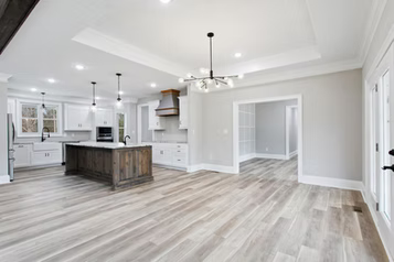 Open-concept kitchen and living area with wood flooring. White cabinets, dark island, and light gray walls.