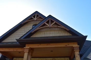 Wooden home exterior with gable roof and decorative trim against a blue sky.