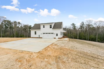 White house with a concrete driveway and undeveloped yard under a blue sky.