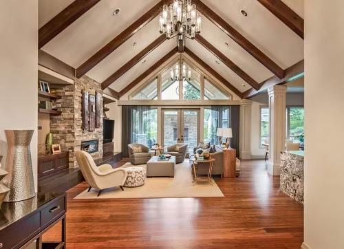 Spacious living room with vaulted ceiling, wood beams, stone fireplace, and floor-to-ceiling windows.