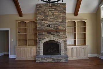 Stone fireplace flanked by built-in bookshelves. Dark wood floor and tan walls.
