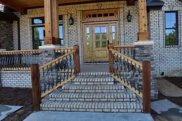 Brick home entrance with steps, wood door, railing, and columns.