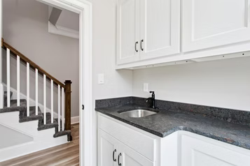 White cabinets and dark countertop in a home, with a staircase visible in the background.