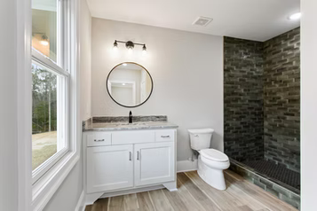 Bathroom with white vanity, round mirror, dark shower, and large window.