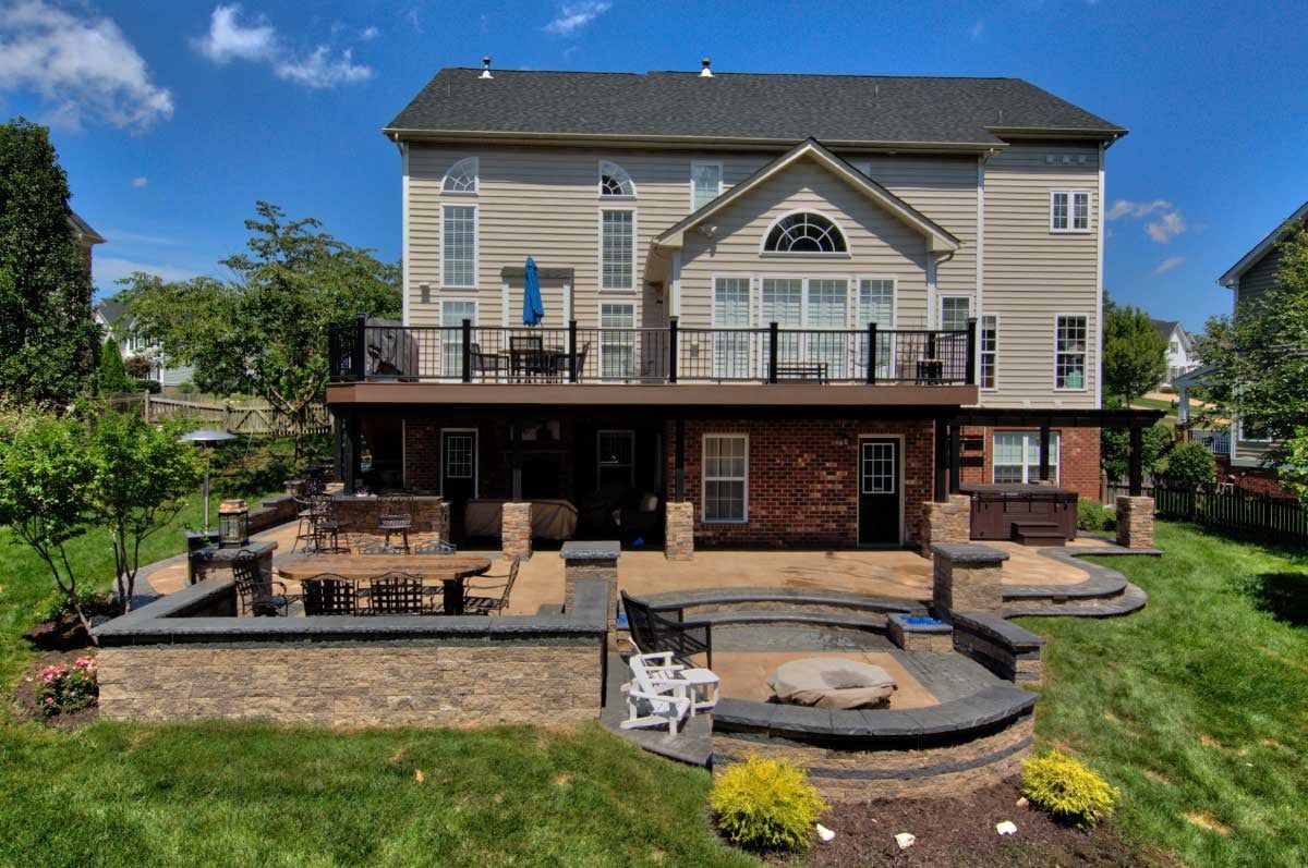 Back of a multi-story house with a large deck and patio overlooking a grassy backyard.