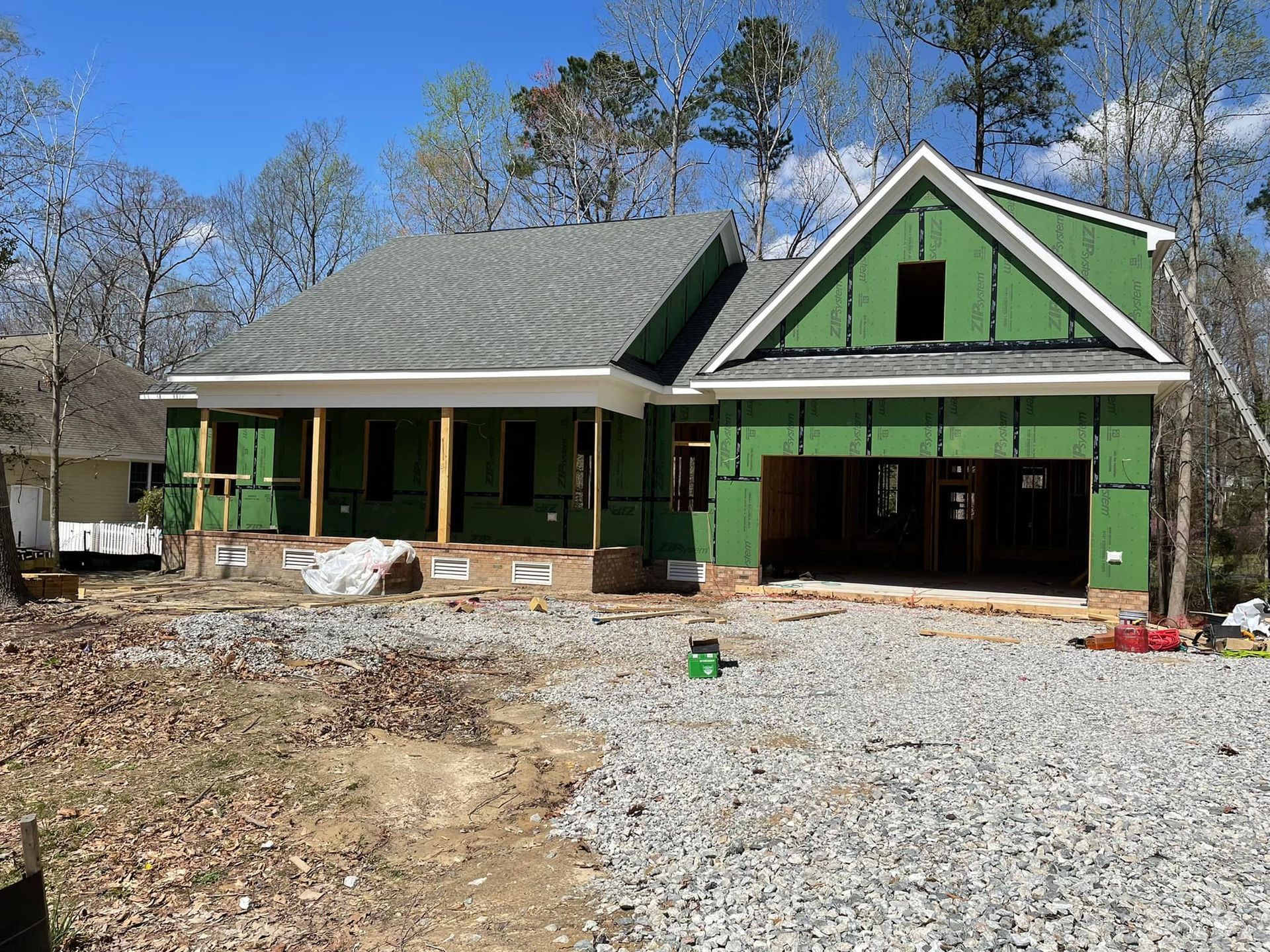 New house under construction with green exterior, garage, and porch in a wooded area.