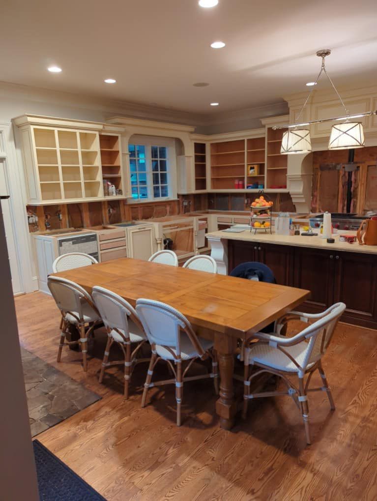Kitchen undergoing renovation, with a large wooden table and chairs, cabinetry, and unfinished construction.