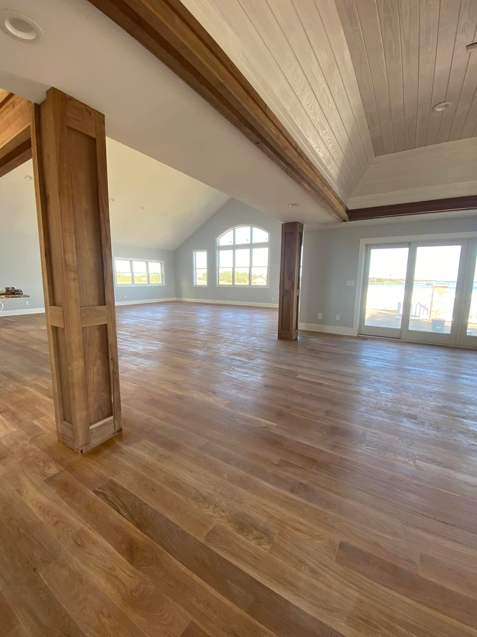 Spacious interior with wood floors, beams, and columns. Large windows and doors lead outside, with a white ceiling.