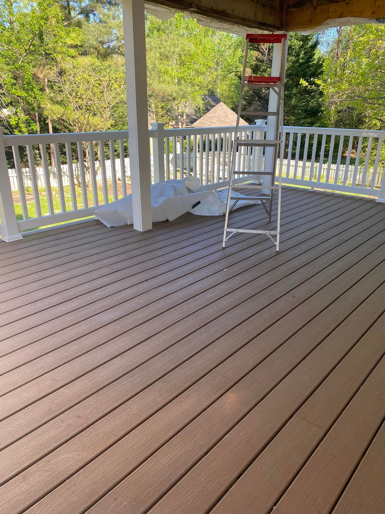 Deck with brown planks, white railing, and ladder. Sunlight streams through trees in the background.