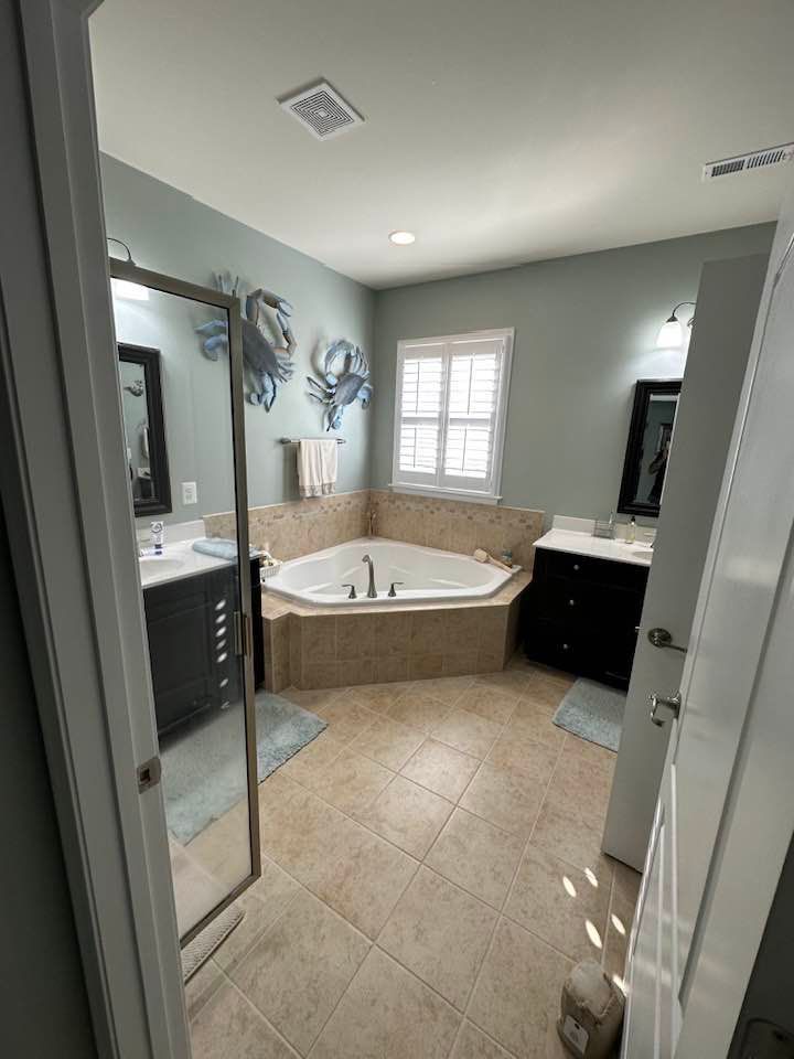 Bathroom with dual vanities, corner jacuzzi tub, light blue walls, and a window.