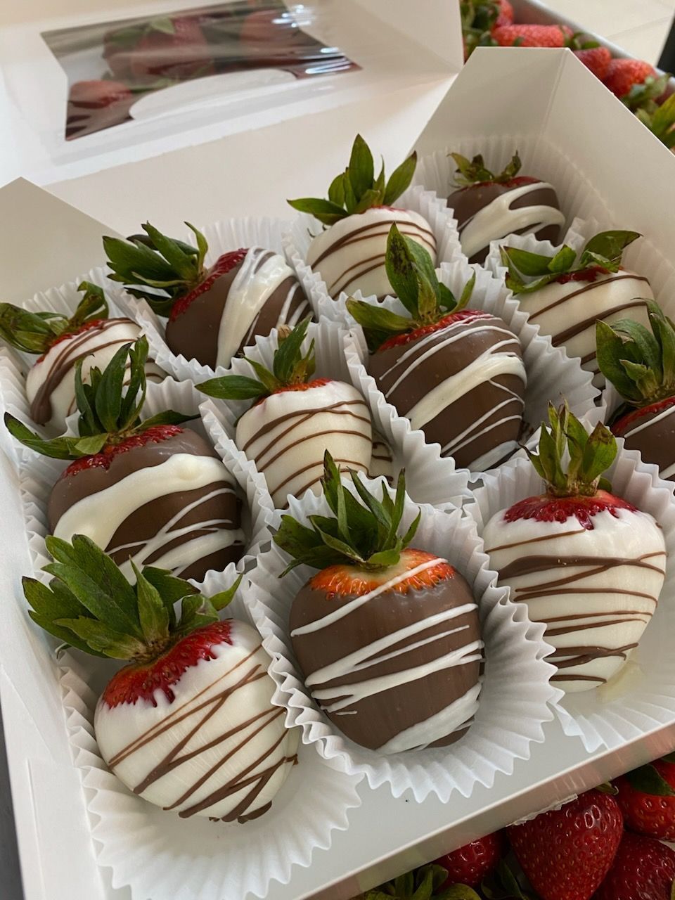 A gift box filled with fresh strawberries dipped in milk and white chocolate with decorative drizzles.