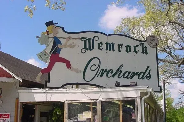 A sign for Wemrock Orchards featuring a cartoon figure walking with a sack over their shoulder against a blue sky.