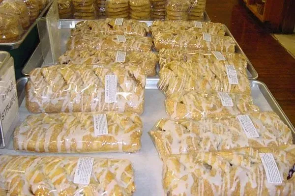 Trays of braided, glazed pastries wrapped in clear plastic arranged on shelves in a bakery.