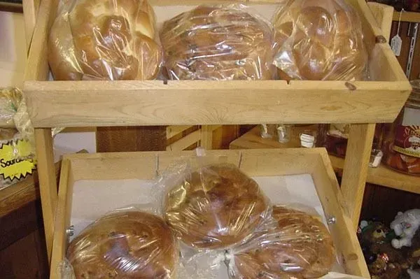 Two wooden shelves displaying several golden-brown, braided loaves of bread individually wrapped in clear plastic bags.