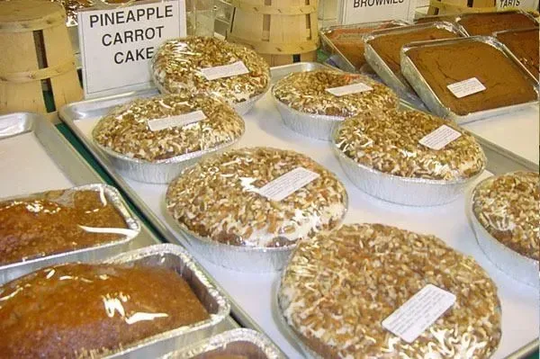 A display of round pineapple carrot cakes in foil tins alongside rectangular loaves on a white table.