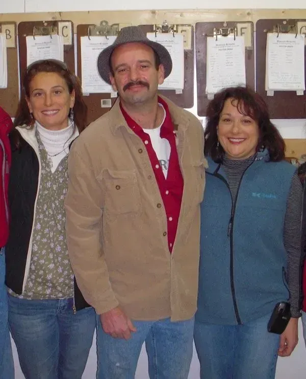 Three people stand in front of a wall with clipboards, smiling for a group photo indoors.